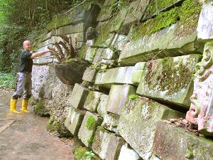 Klaus Ritter steht in der Starzel. Mit einem Zollstock zeigt er, wo sich der Bauch der  Mauer aus alten  Grabsteinen zu wölben beginnt.  Fotos: Dick Foto: Schwarzwälder-Bote