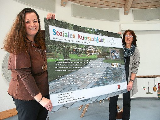 Kathrin Bauer (links) und Sabine Schumacher präsentieren das Plakat, mit dem für das soziale Kunstobjekt geworben wird. Fotos: Selent-Witowski Foto: Schwarzwälder-Bote