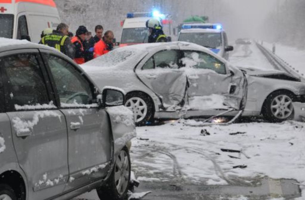 Rettungskräfte stehen am Freitag auf der schneebedeckten B 292 bei Walldorf nach einem Unfall hinter zwei beschädigten Fahrzeugen.