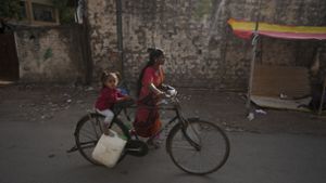 Eine Frau mit einem Kind transportiert Wasser mit einem Fahrrad aus einem öffentlichen Wasserhahn in einem Slumgebiet der indischen Stadt. In Südasien leiden weltweit am meisten Kinder an Wasserknappheit. Foto: AP/dpa/Mahesh Kumar A.