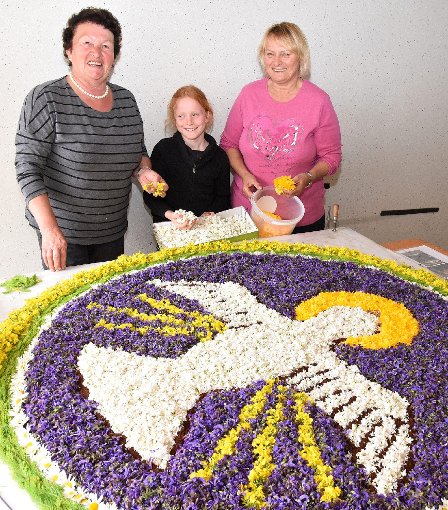 Elisabeth Bok (links) und Brunhilde Enderle von der Frauengruppe und  Lisa-Marie Bok (9) präsentieren den großen Blütenteppich mit dem Motiv Taube. Foto: Schwarzwälder-Bote