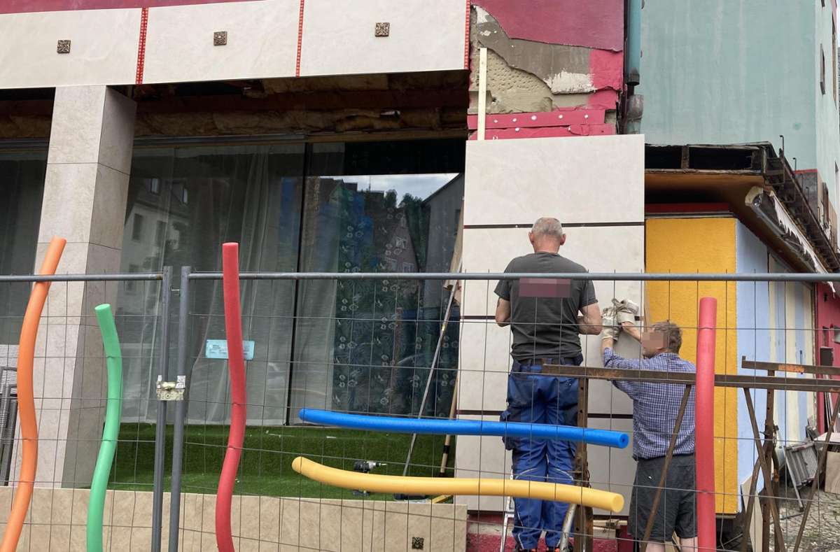 Der Bauzaun ist mit bunten Schwimmnudeln verziert, während Bauarbeiter die Fassadenplatten anbringen Foto: Lück