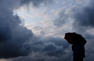 Ein Mann geht mit einem Regenschirm vor aufziehenden dunklen Wolken spazieren. Foto: dpa/Martin Gerten