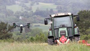 Eine Drohne schwebt über der Wiese, dahinter wartet der Landwirt ab, wann er mähen kann Foto: Jauch