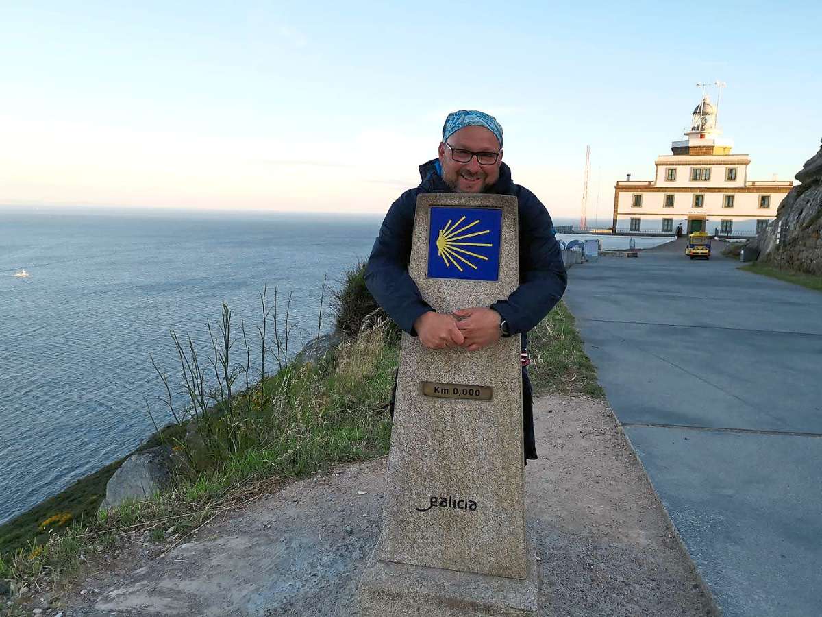 Roberto Chiari steht am Null-Stein am Kap Finisterre am Ende der Welt. Er umarmt den Stein mit der Jakobsmuschel.