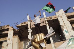 Über den Trümmern von Tripolis schwenkt ein Gaddafi-Gegner die libysche Flagge. Foto: EPA