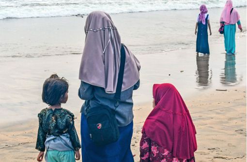 Frauen mit Kopftüchern am Strand in Kuta auf Bali. In Indonesien herrschen teilweise strikte Kleiderordnungen für Frauen. Foto: imago//Winfried Rothermel