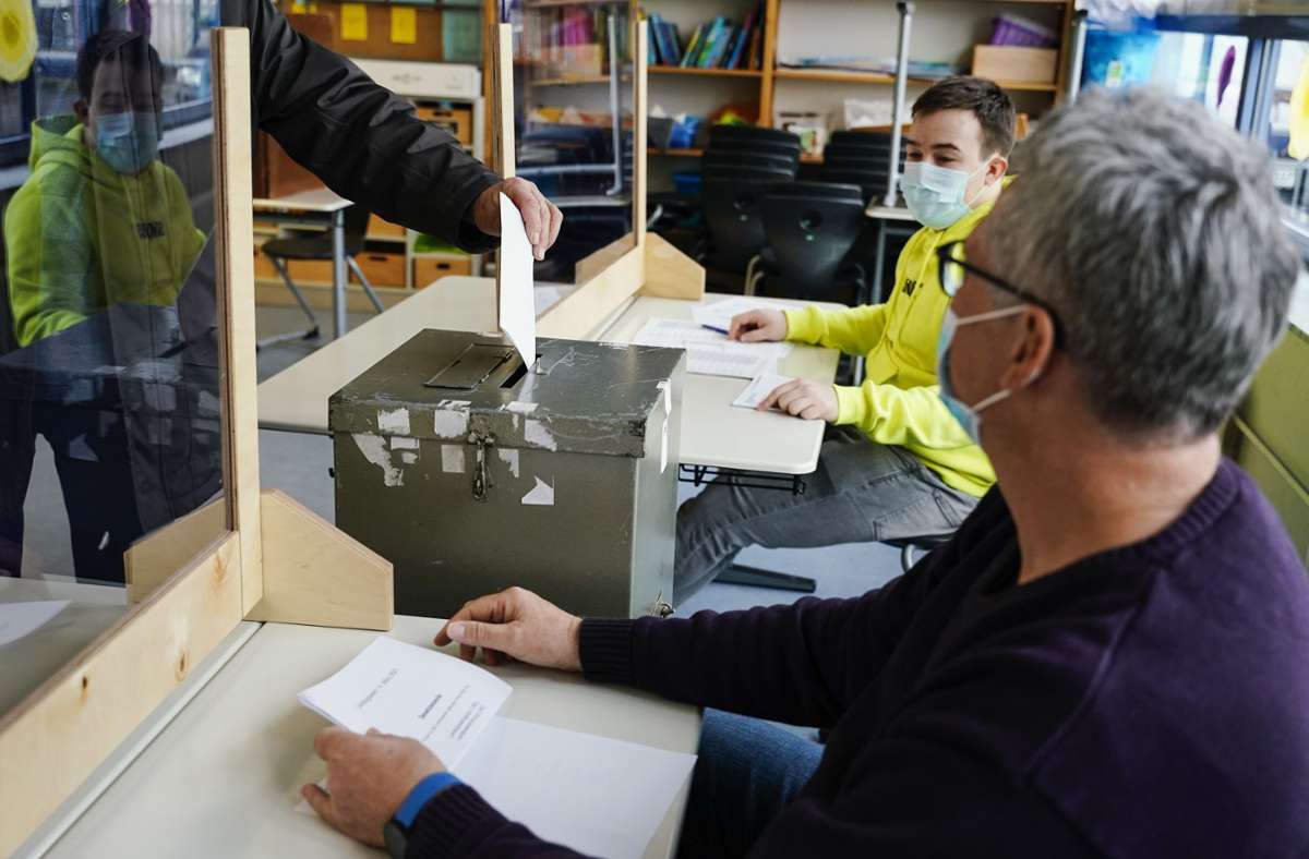 ... ein Wähler steht hinter einer Plexiglasscheibe und wirft seinen Stimmzettel in die Wahlurne.