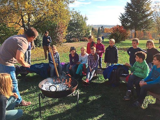 Die vierten Klassen sitzen mit Achim Grabert  an einem Feuer, in dem die selbst geernteten Kartoffeln liegen.  Foto: Schule Foto: Schwarzwälder-Bote