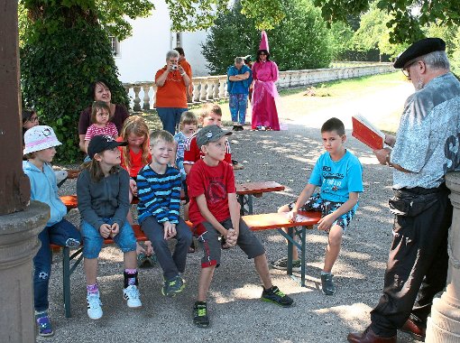 Gebannt lauschen die Kinder im Schlosspark in Geislingen dem Märchenerzähler Markus Maucher, während hinter ihnen eine sehr männlich wirkende gute Fee (Andreas Gulde) wartet. Foto: Leukhardt