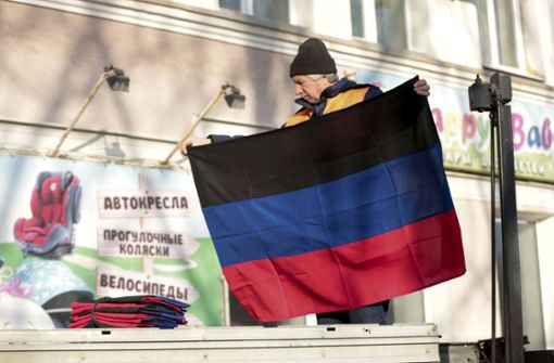 Ein Gemeindearbeiter hält eine Flagge der international nicht anerkannten Volksrepublik Donezk, die an einem Gebäude in der gleichnamigen Stadt angebracht werden soll. (Archivbild) Foto: dpa/Alexei Alexandrov
