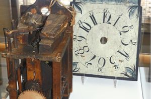Eine rätselhafte Kuckucksuhr mit Holzrädern ist das Objekt des Monats Dezember im Uhrenmuseum. Werk und Schild sind getrennt ausgestellt, da anzunehmen ist, dass das Schild erst später nach der 1793/95 gefertigten Uhr entstand. Foto: Kouba