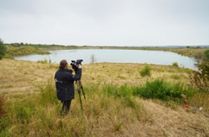 Ein Kameramann filmt am Ufer des Teufelsees im hessischen Wetteraukreis, in dem die Leiche der 14-jährigen Ayleen gefunden wurde. (Archivbild) Foto: dpa/Frank Rumpenhorst
