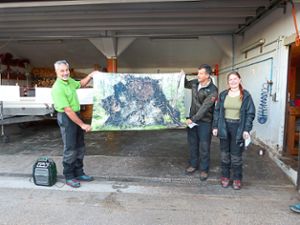 Meinrad Schweikart (links) und Björn Waidelich überreichten der Forstwirtin Tabea Nachbar für ihren guten Abschluss ein Handtuch mit einem Bildmotiv, das sie vor einem großen Wurzelteller zeigt. Foto: Celine Urban