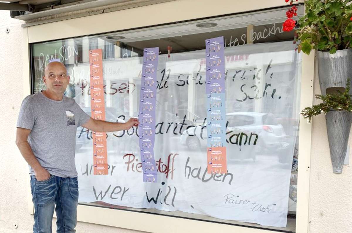 Rainer Lüthy hält eine der gebastelten Aufhänger in der Hand, die ein Unbekannter an das Schaufenster der Pension geklebt hat. Eine Reaktion auf das Impfplakat des ehmaligen Bäckermeisters. Foto: Alt