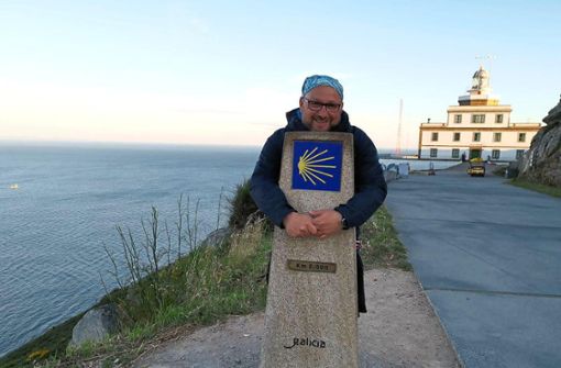 Roberto Chiari steht am Null-Stein am Kap Finisterre am Ende der Welt. Er umarmt den Stein mit der Jakobsmuschel. Foto: Chiari