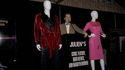Ein Auktionator  bietet Hugh Hefners Smoking-Jacket und Marilyn Monroes rosa Pucci-Kleid bei der Versteigerung in Los Angeles zum Verkauf an. Foto: -/Julien’s Auctions/dpa