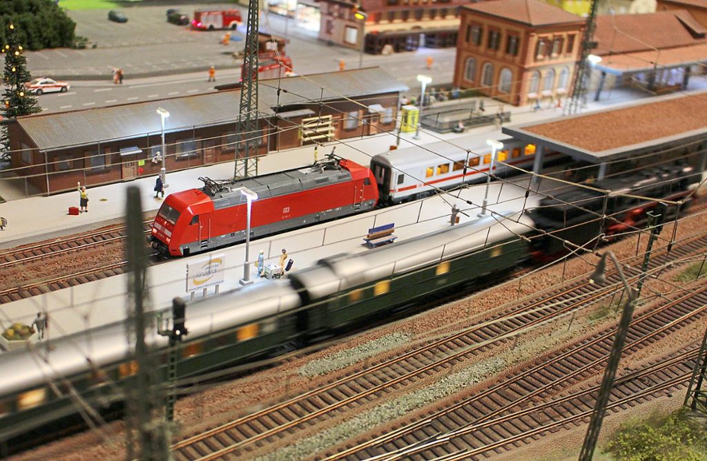 Blick auf den Hausacher Bahnhof, in den gerade eine Dampflok mit Personenwagen einfährt  – im Hintergrund sind die erleuchteten Fenster des Modelleisenbahn-Domizils zu sehen.