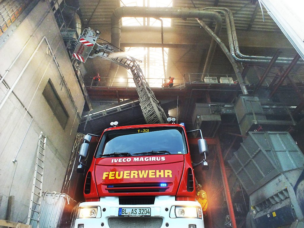 Feuerwehreinsatz in Halle drei der Firma Korn.  Unfallort ist die Empore (links); mit Hilfe der Drehleiter wird der Verletzte hinunter aufs Straßenniveau und ins Freie gebracht.