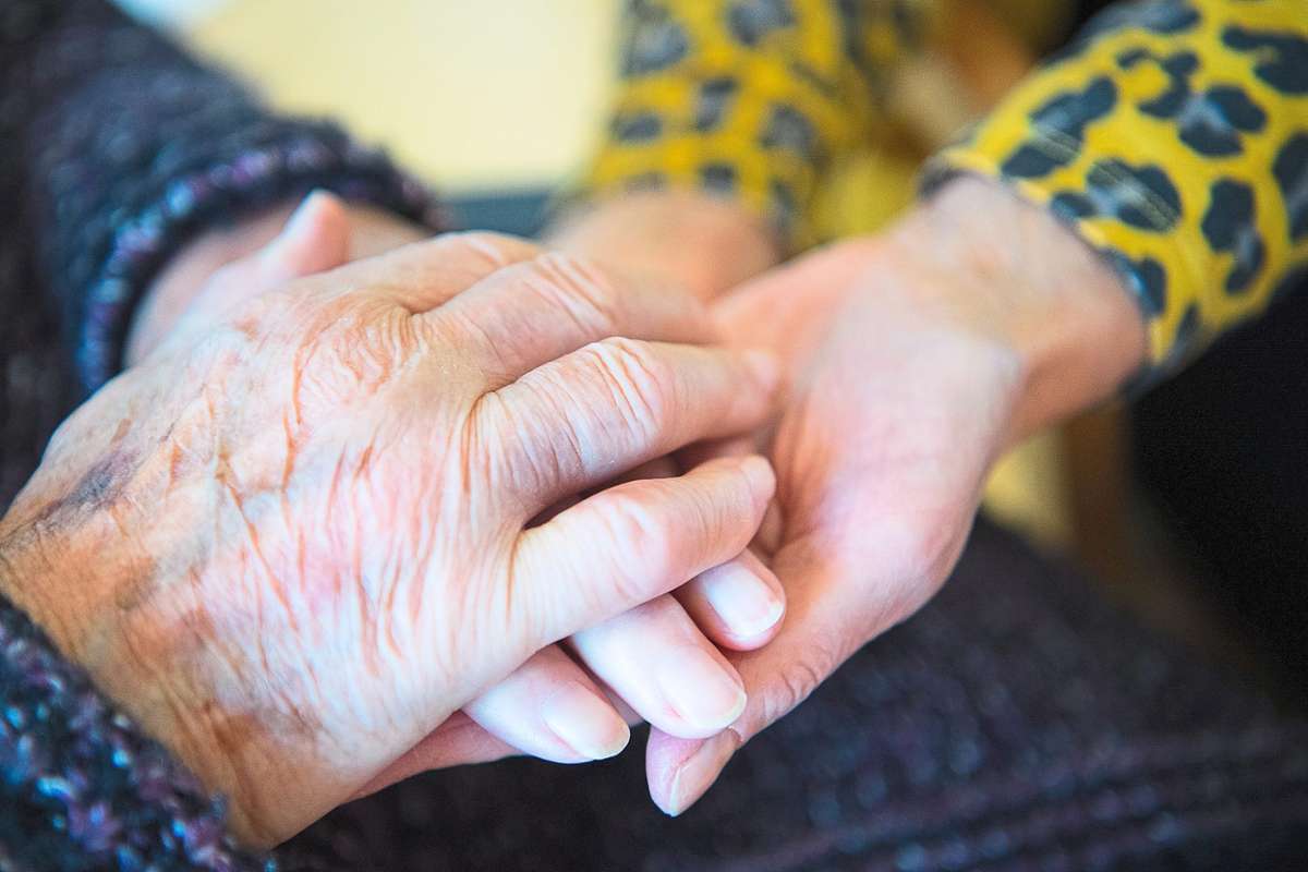 Eine Besucherin einer Pflegeeinrichtung und eine Bewohnerin halten Hände. Foto: Tom Weller/dpa